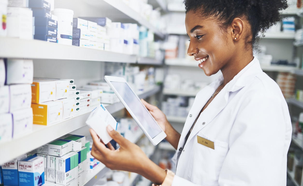 female pharmacy employee looking at a tablet while holding meds