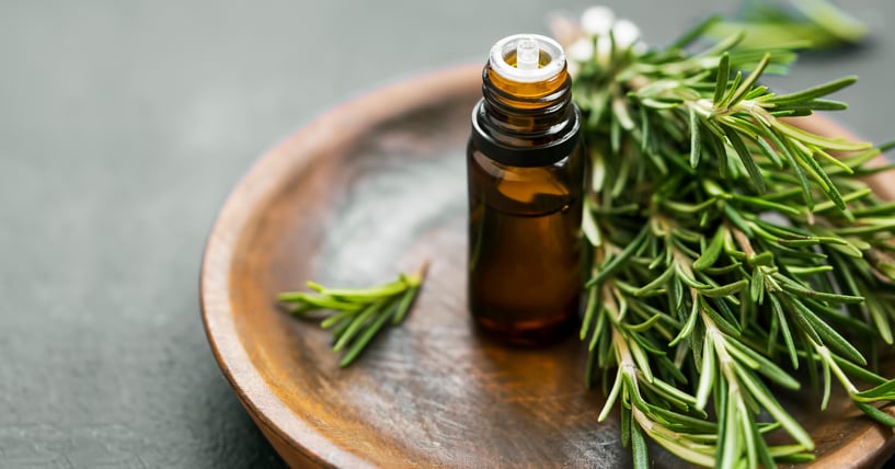 rosemary sprigs on a wooden plate with a small tube of oil