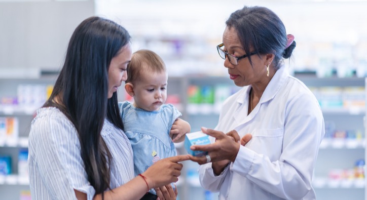 young woman holding a baby while talking to a female pharmacist